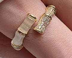 Close-up of a hand wearing two gold rings on a neutral background